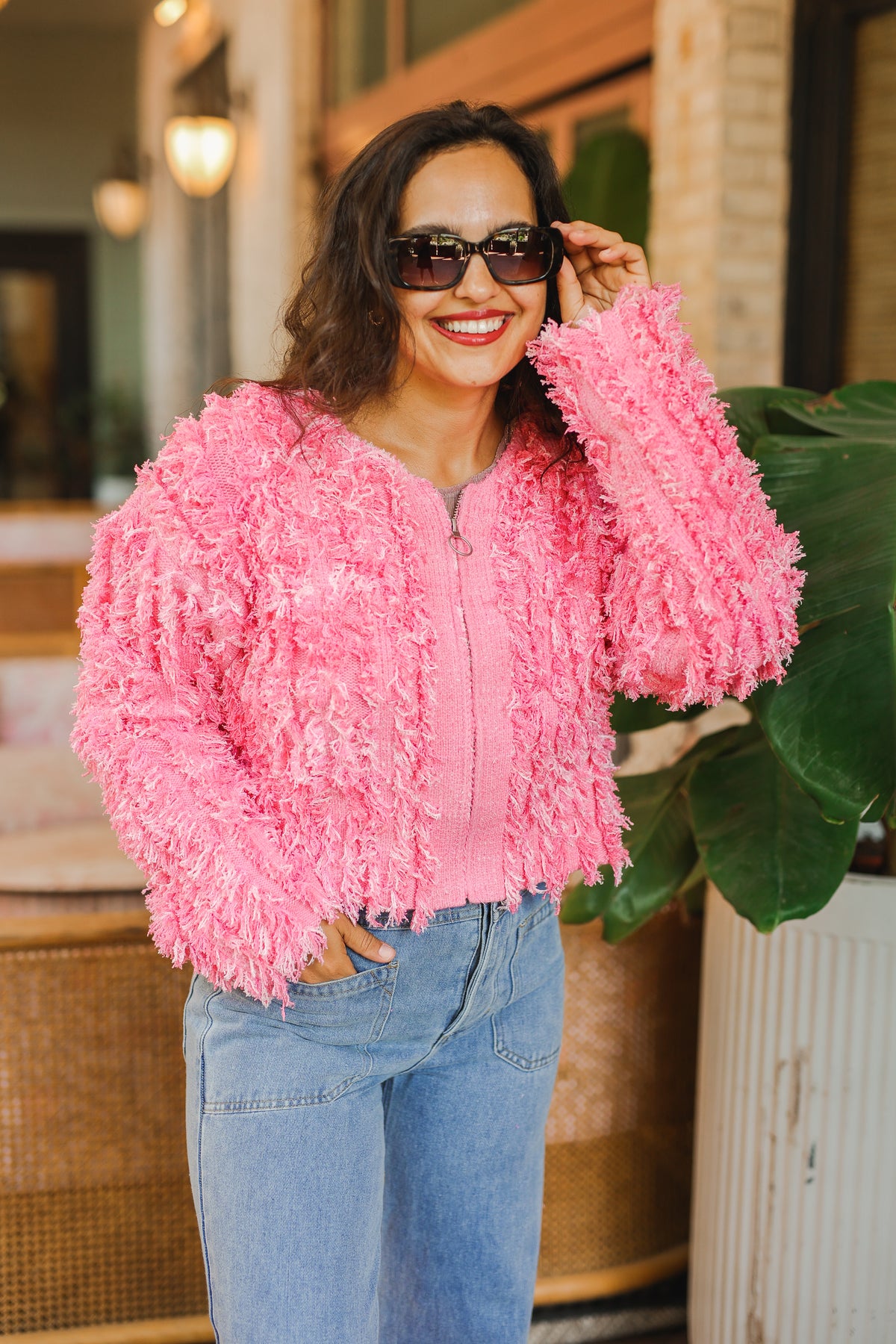 Woman wearing a pink fluffy jacket and sunglasses outdoors.