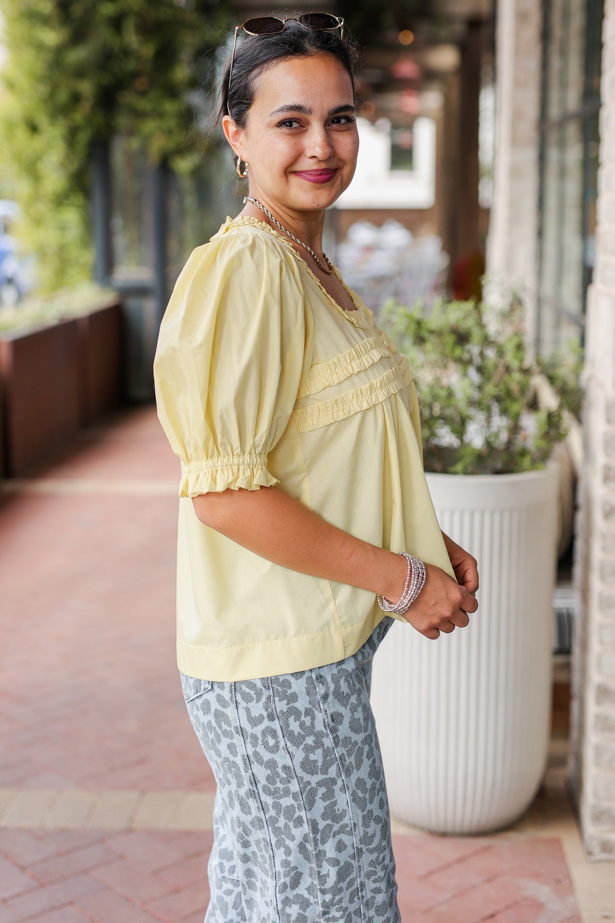 Woman wearing a light yellow blouse with puff sleeves and leopard print pants standing outdoors.