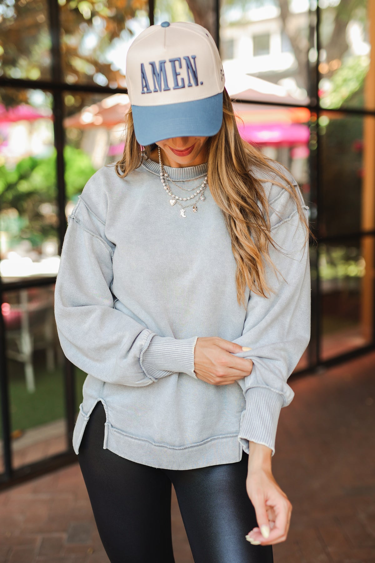 Person wearing a light gray sweatshirt and black leggings with a cap indoors.