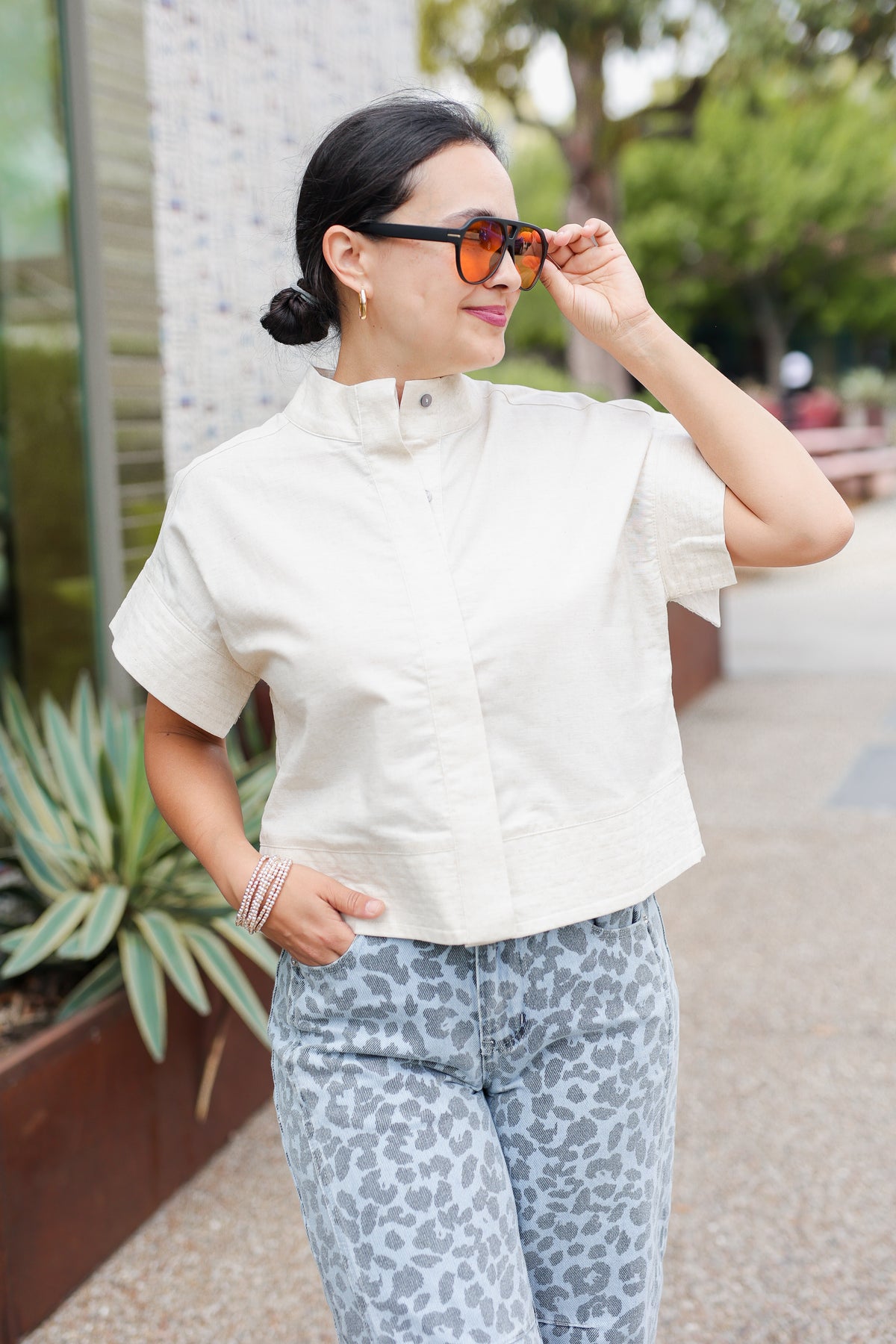Woman wearing a white blouse and patterned pants outdoors.
