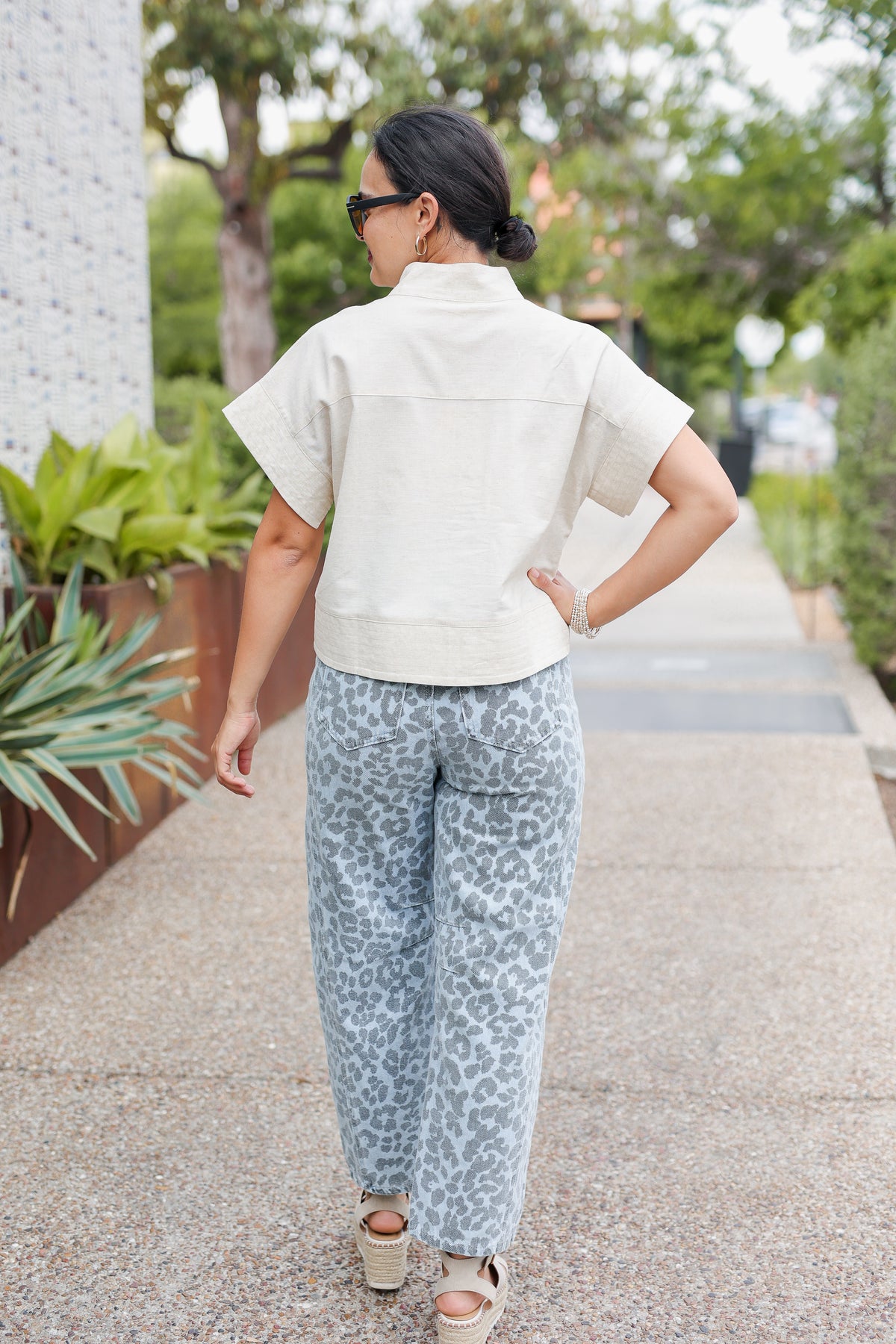 Woman walking outdoors wearing a light-colored top and blue patterned pants.