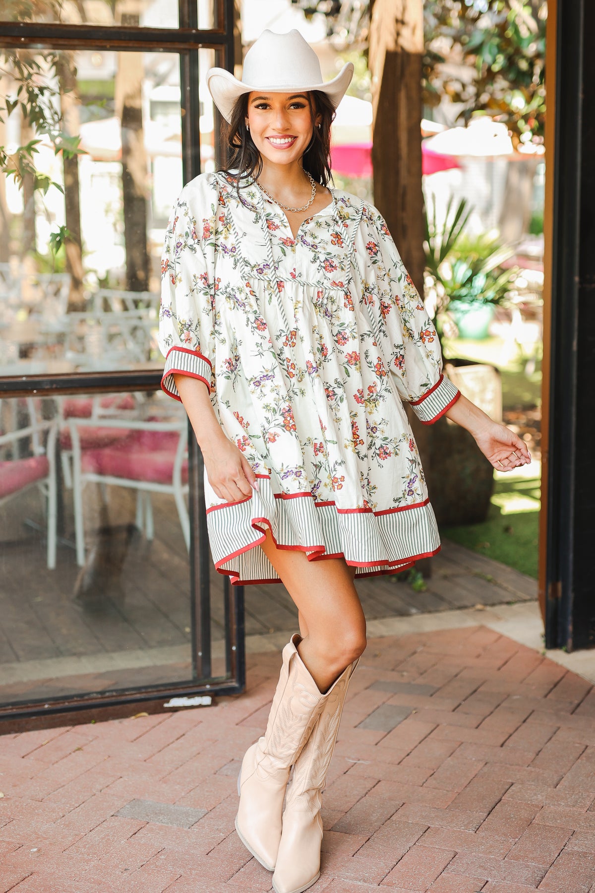 Woman in a floral dress and cowboy boots standing outside a building.