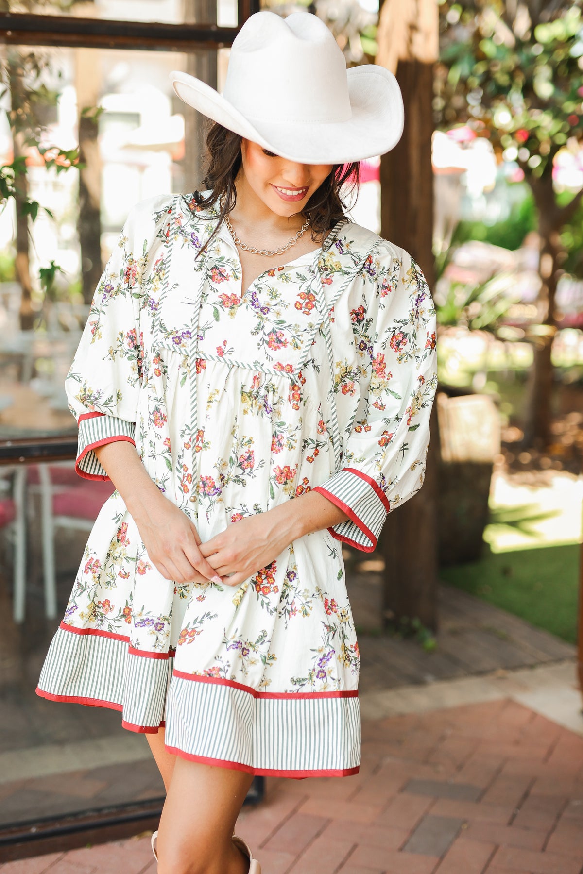 Woman wearing a floral dress with red trim and a white hat outdoors.