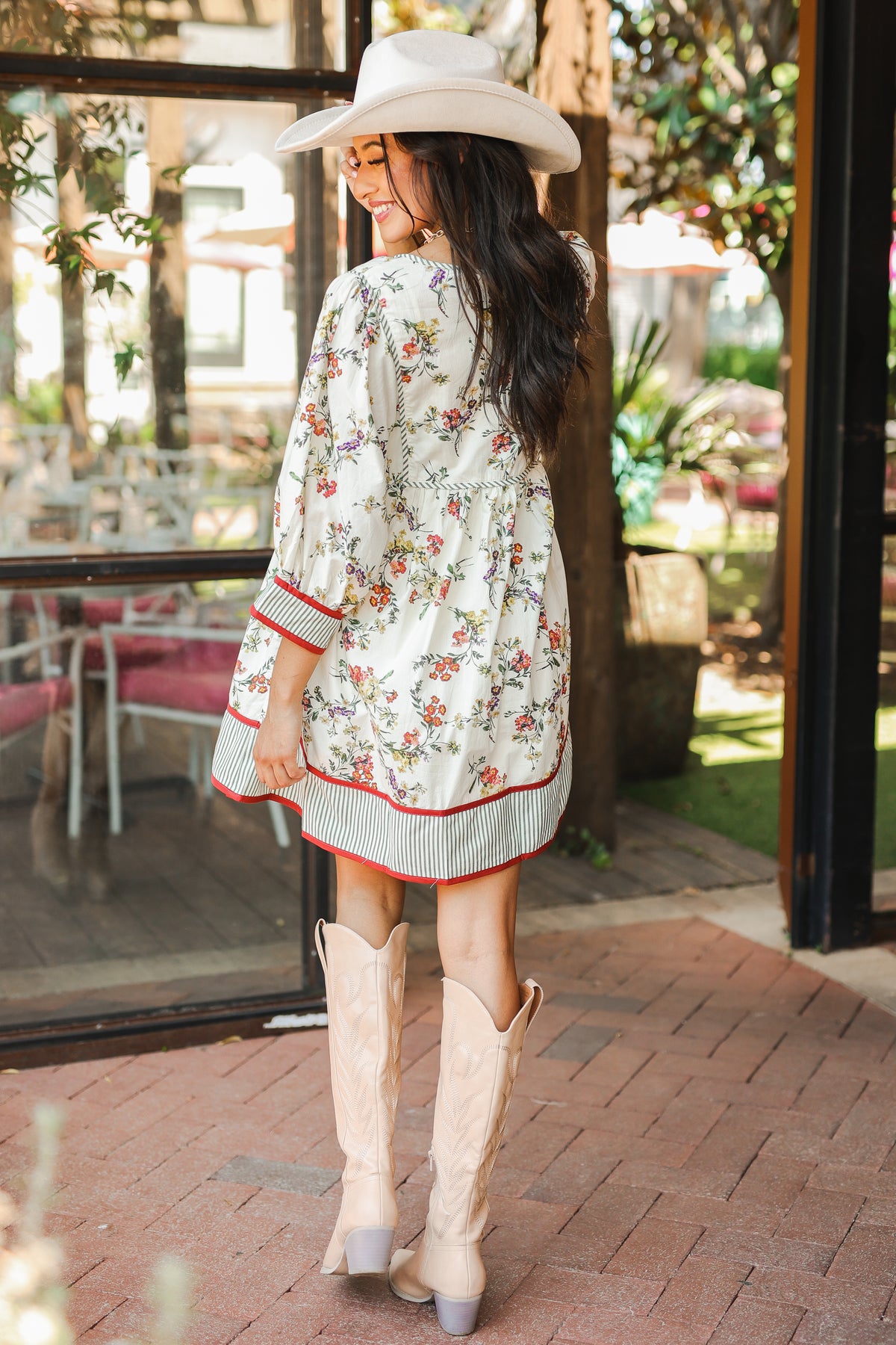 Woman in a floral dress and cowboy boots standing in an outdoor setting.