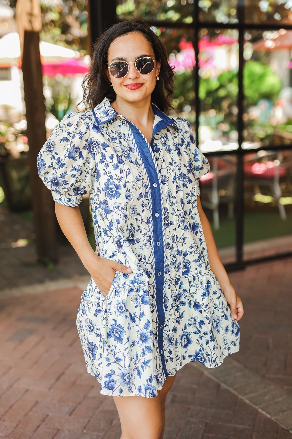 Woman wearing a blue floral dress with sunglasses outdoors.