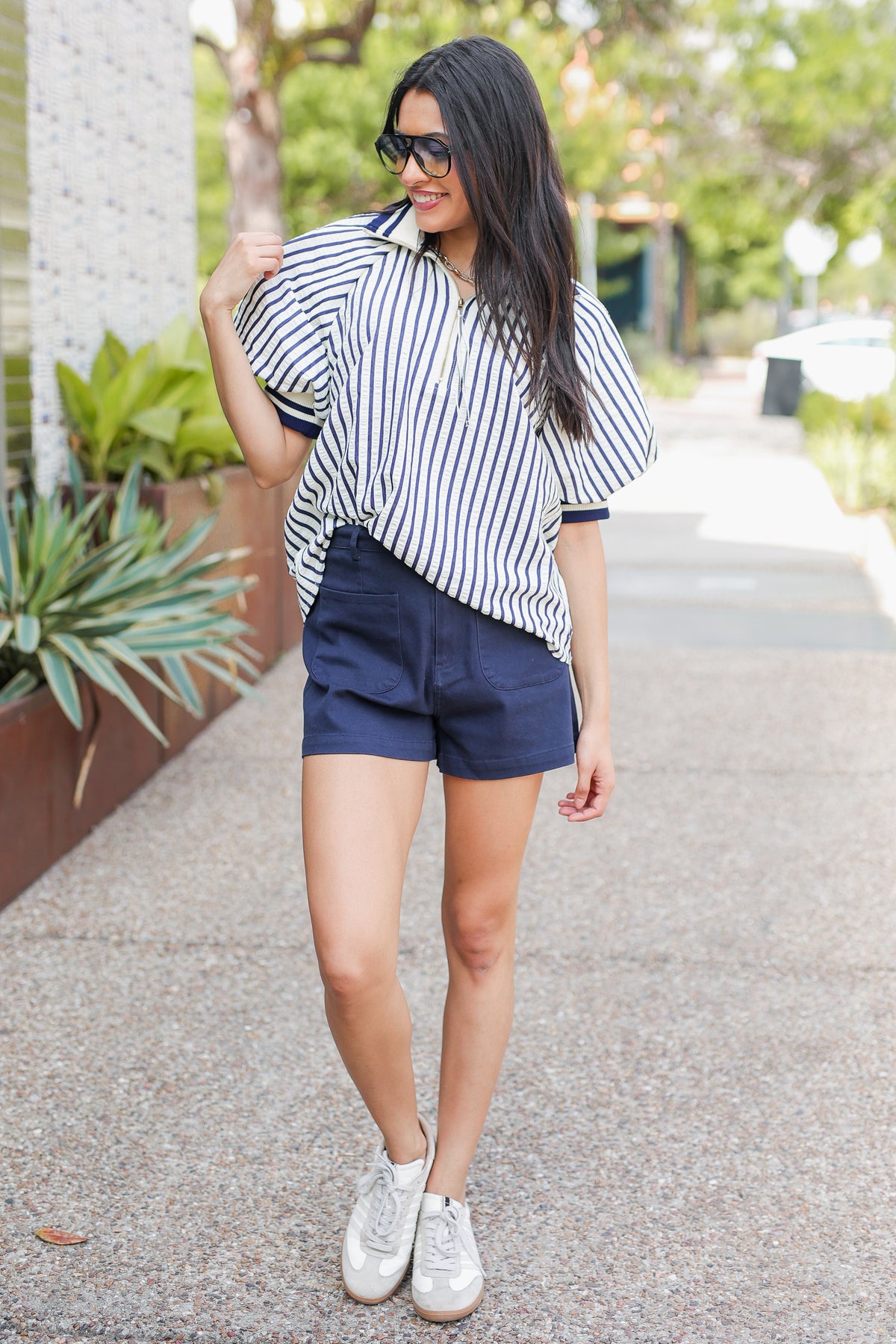 Woman wearing a striped shirt and shorts standing outdoors.