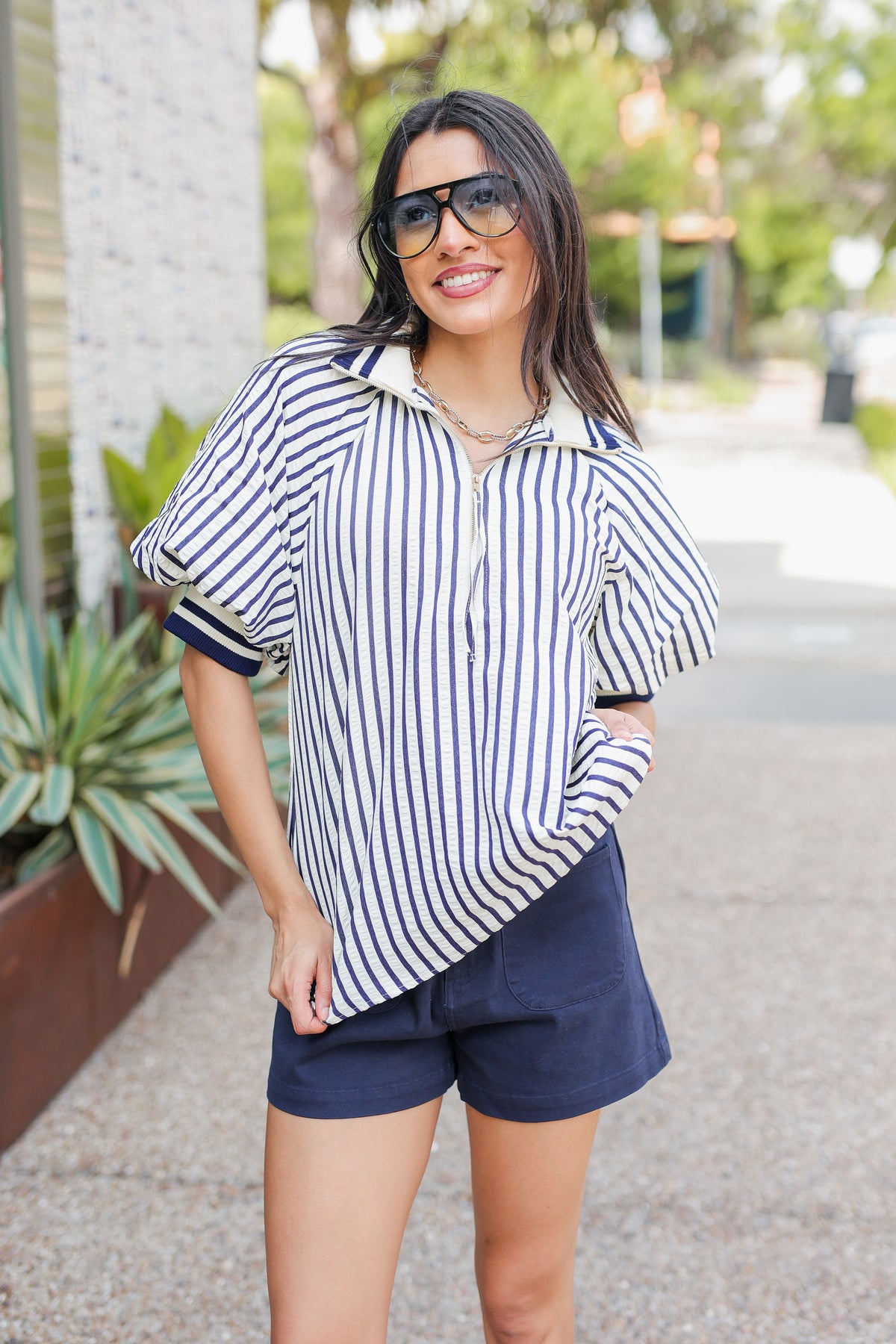 Woman wearing a striped shirt and navy shorts on a street.