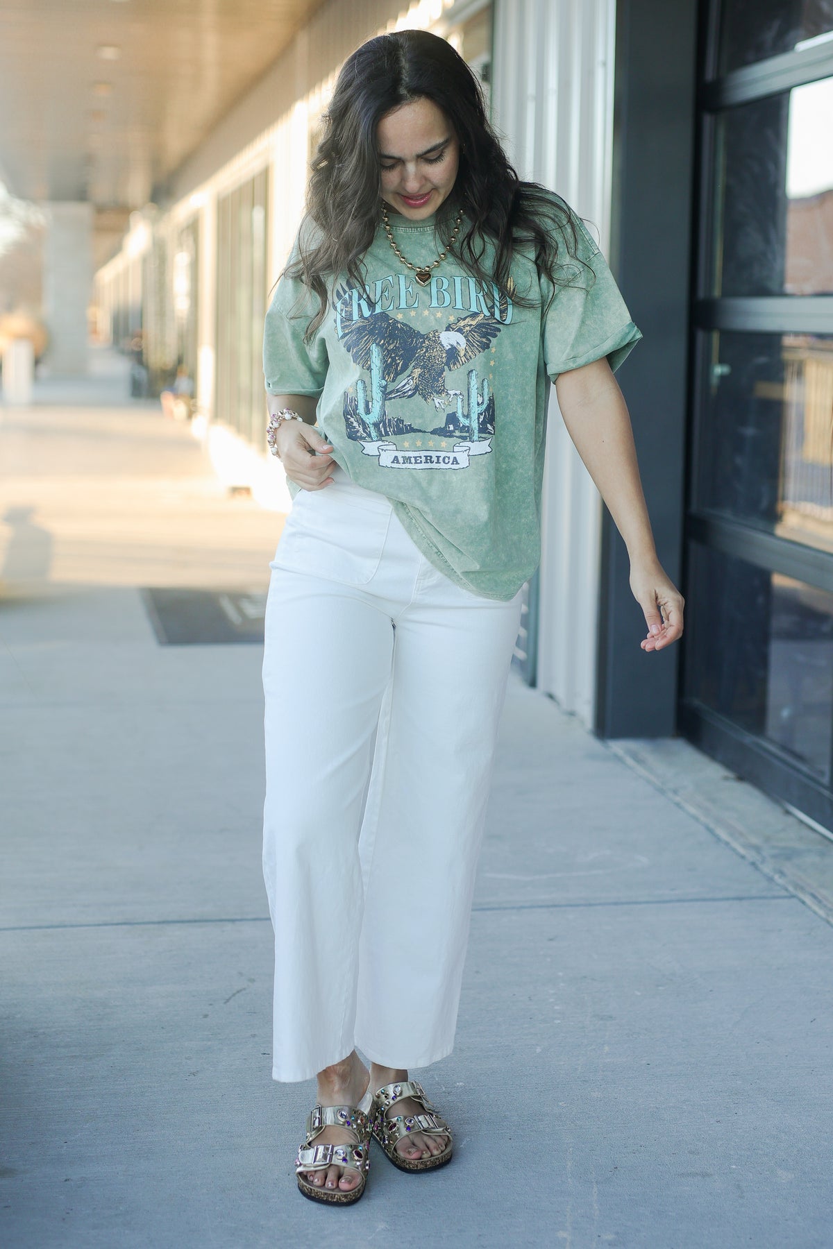 Woman wearing a green graphic t-shirt and white pants on a city street.