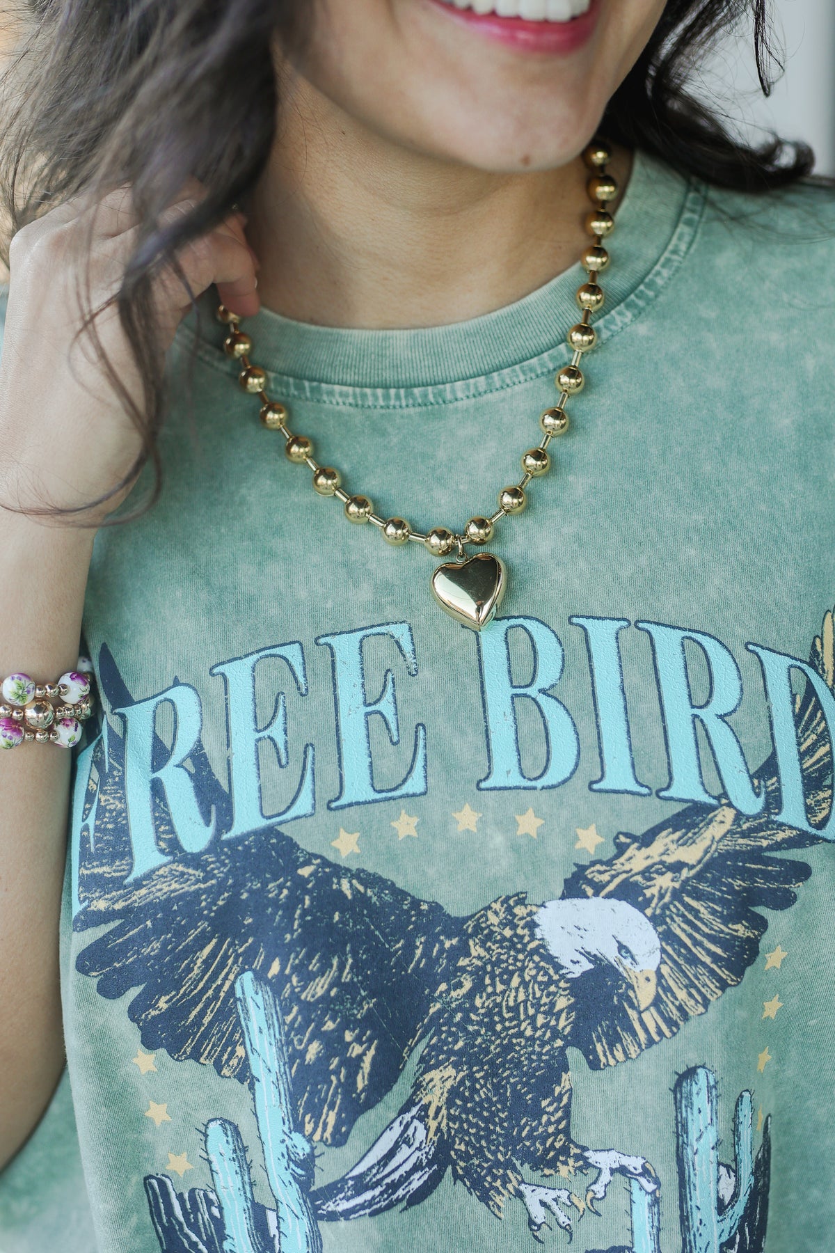 Person wearing a green t-shirt with 'FREE BIRD' and an eagle design, gold necklace, and bracelet.
