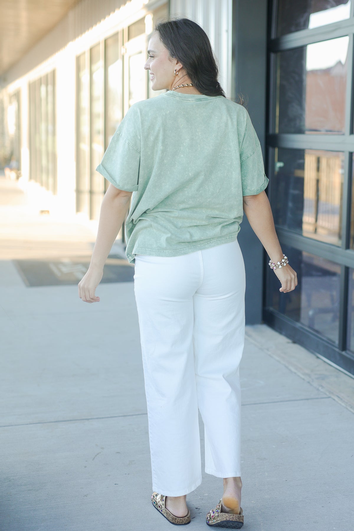 Woman wearing a light green top and white pants walking outdoors.