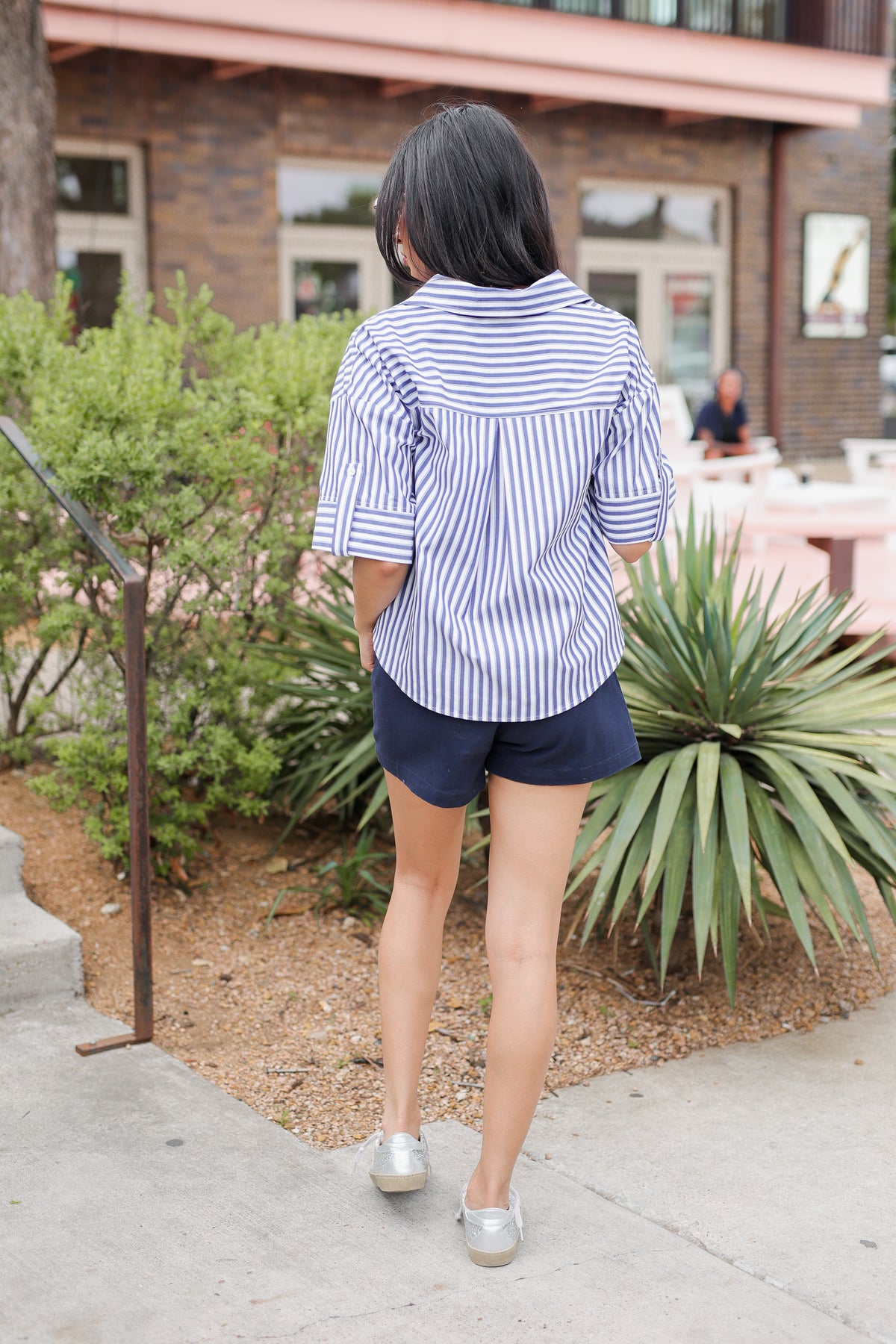 Woman in a striped shirt and shorts standing outdoors near a building.