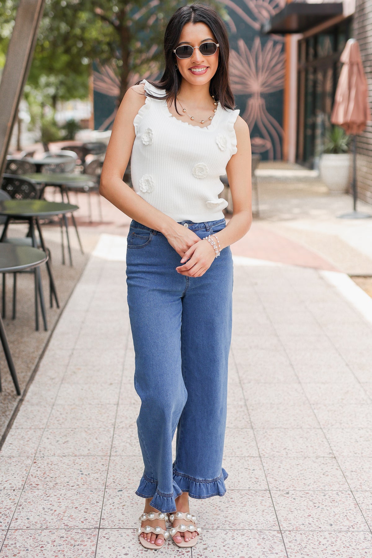Woman wearing a white sleeveless top and blue jeans standing outdoors.