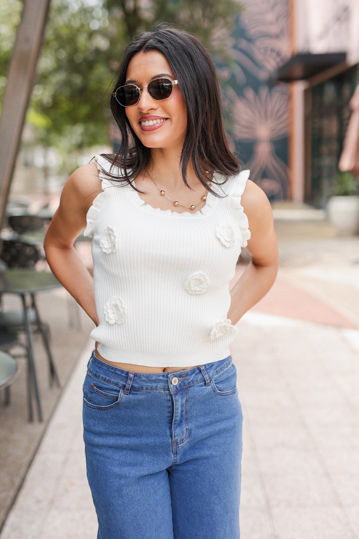 Woman wearing a white sleeveless top and blue jeans outdoors.