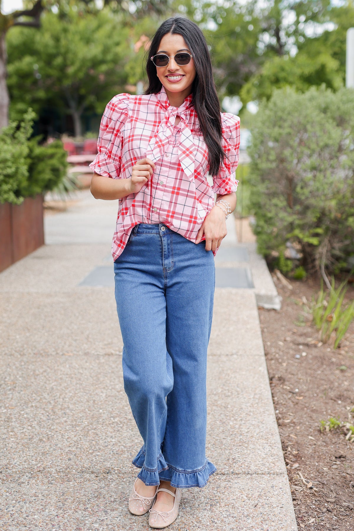 Woman wearing a red plaid shirt and blue jeans standing outdoors.