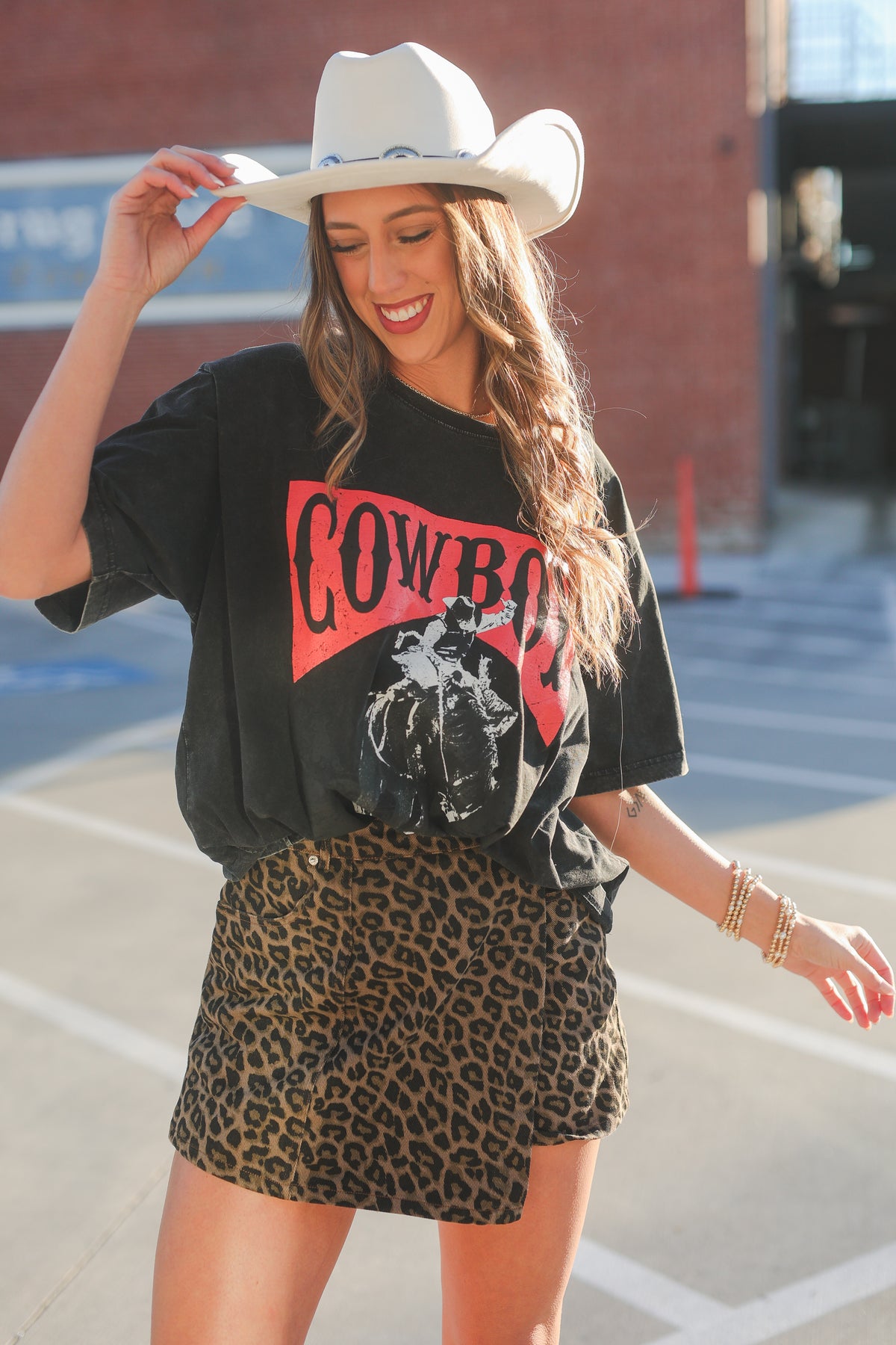 Woman wearing a black t-shirt with 'Cowboy' text and a leopard print skirt, standing on a basketball court.