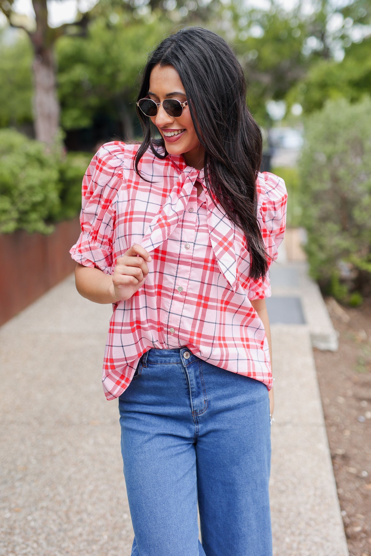 Woman wearing a red plaid shirt and blue jeans outdoors.