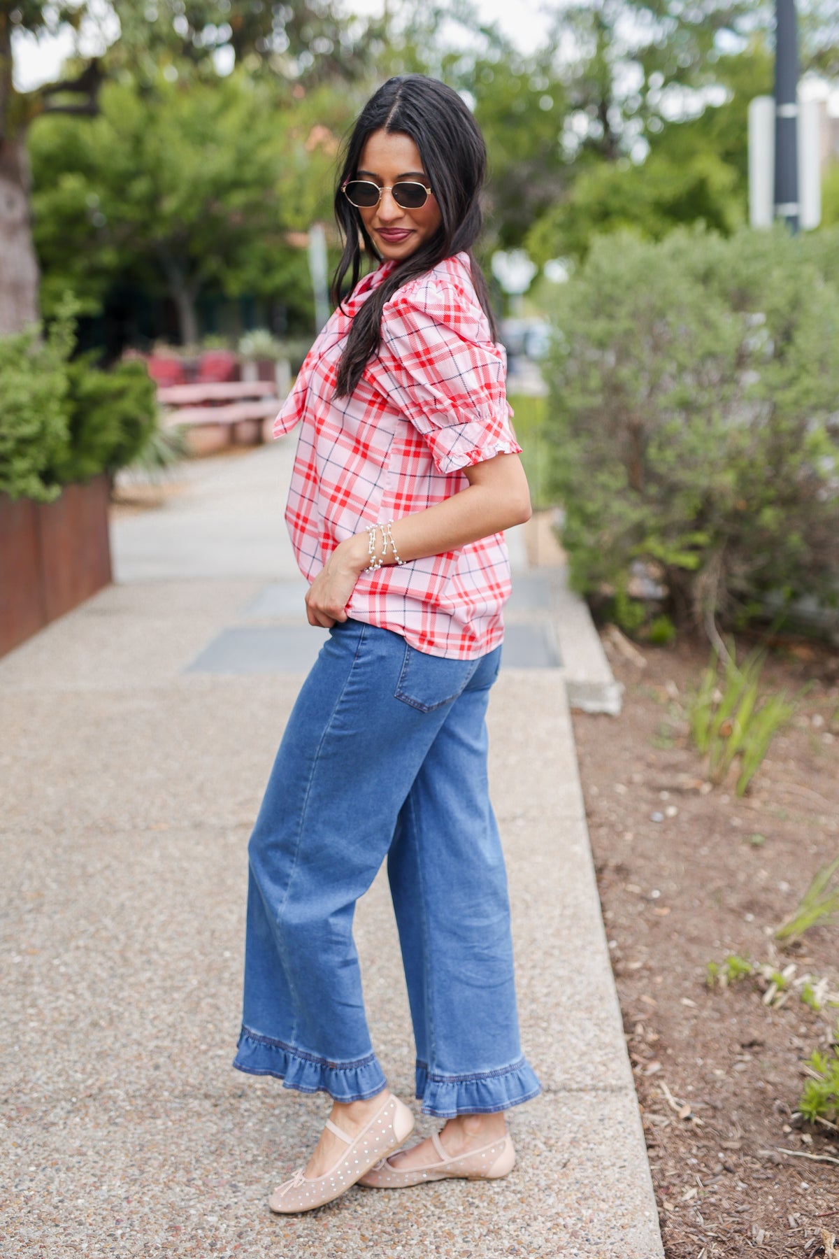 Woman wearing a red plaid shirt and blue jeans standing outdoors.