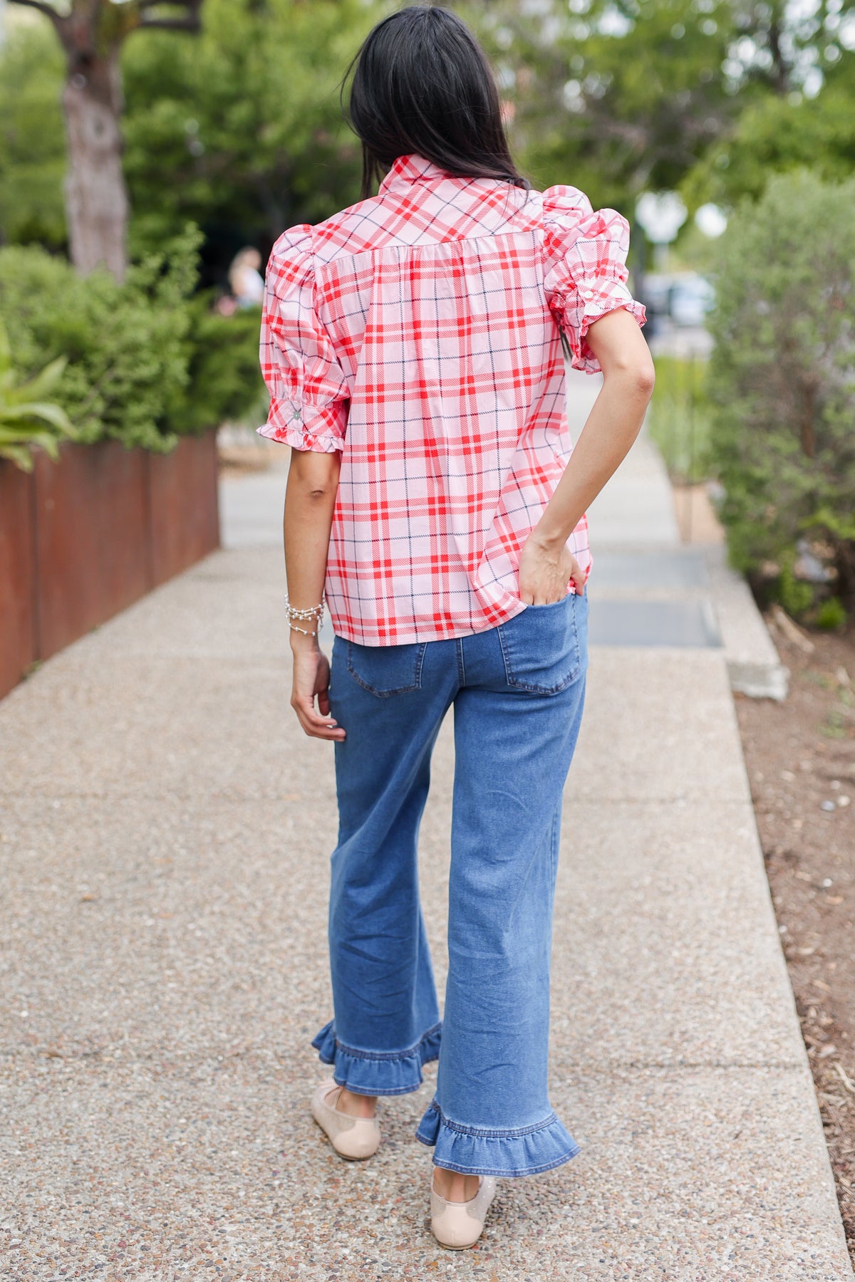 Person wearing a red and white checkered shirt and blue jeans walking outdoors.