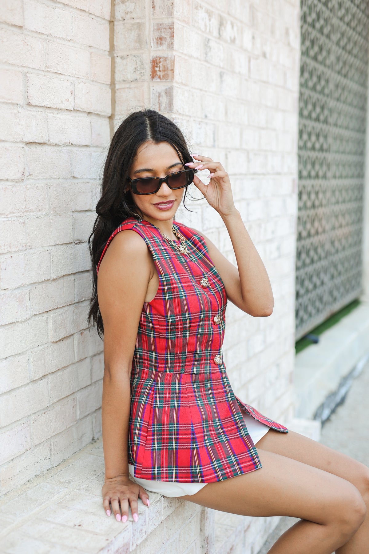 Woman wearing a red plaid dress against a white brick wall.