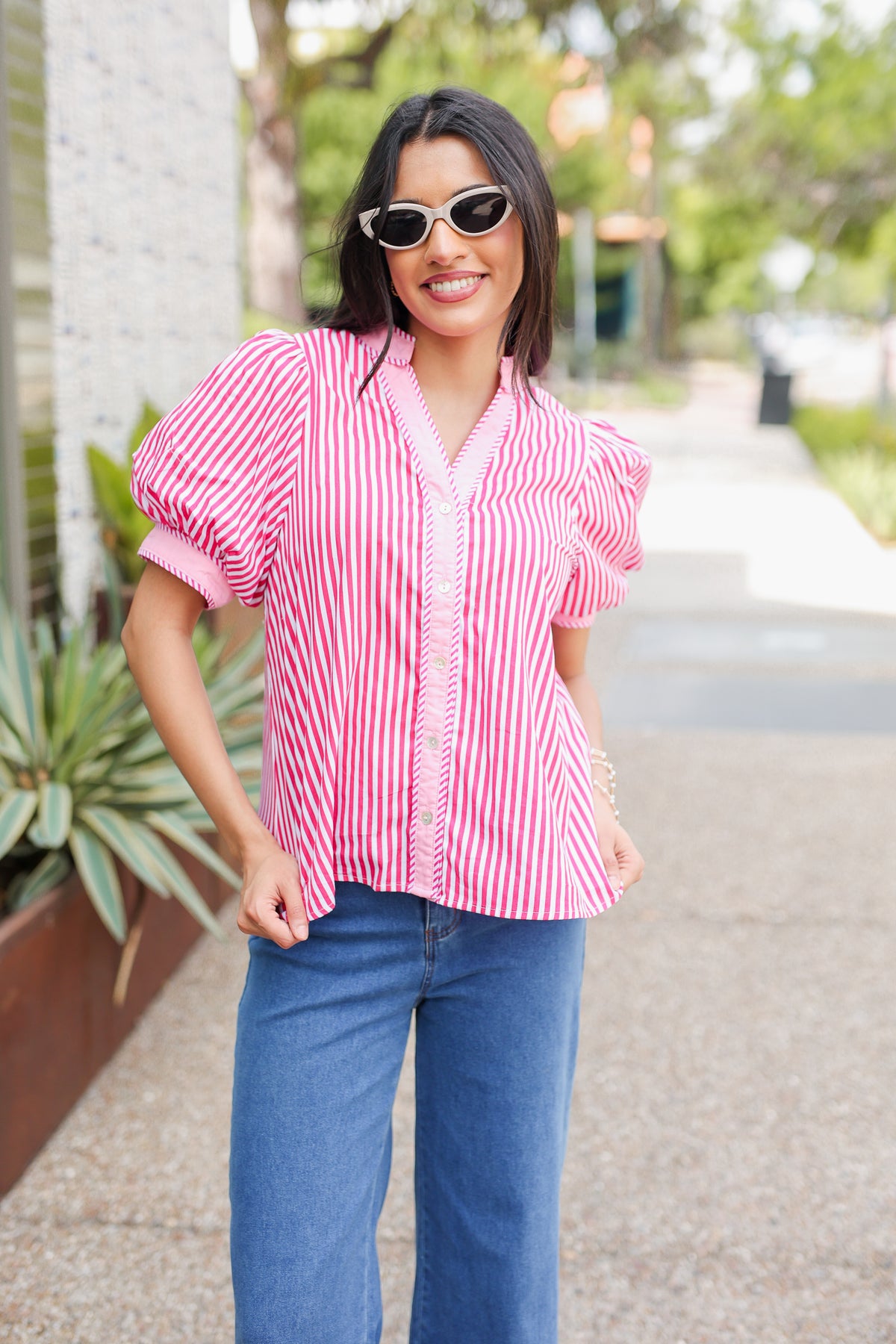 Woman wearing a pink and white striped blouse and blue jeans outdoors.
