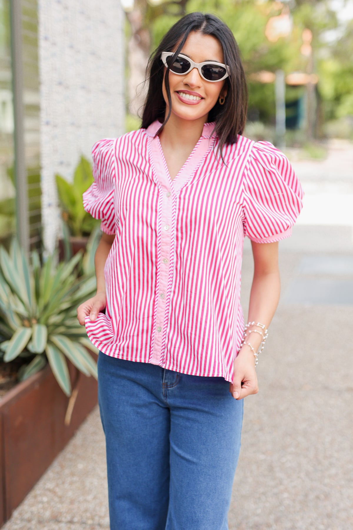 Woman wearing a pink and white striped shirt and blue jeans standing outdoors.