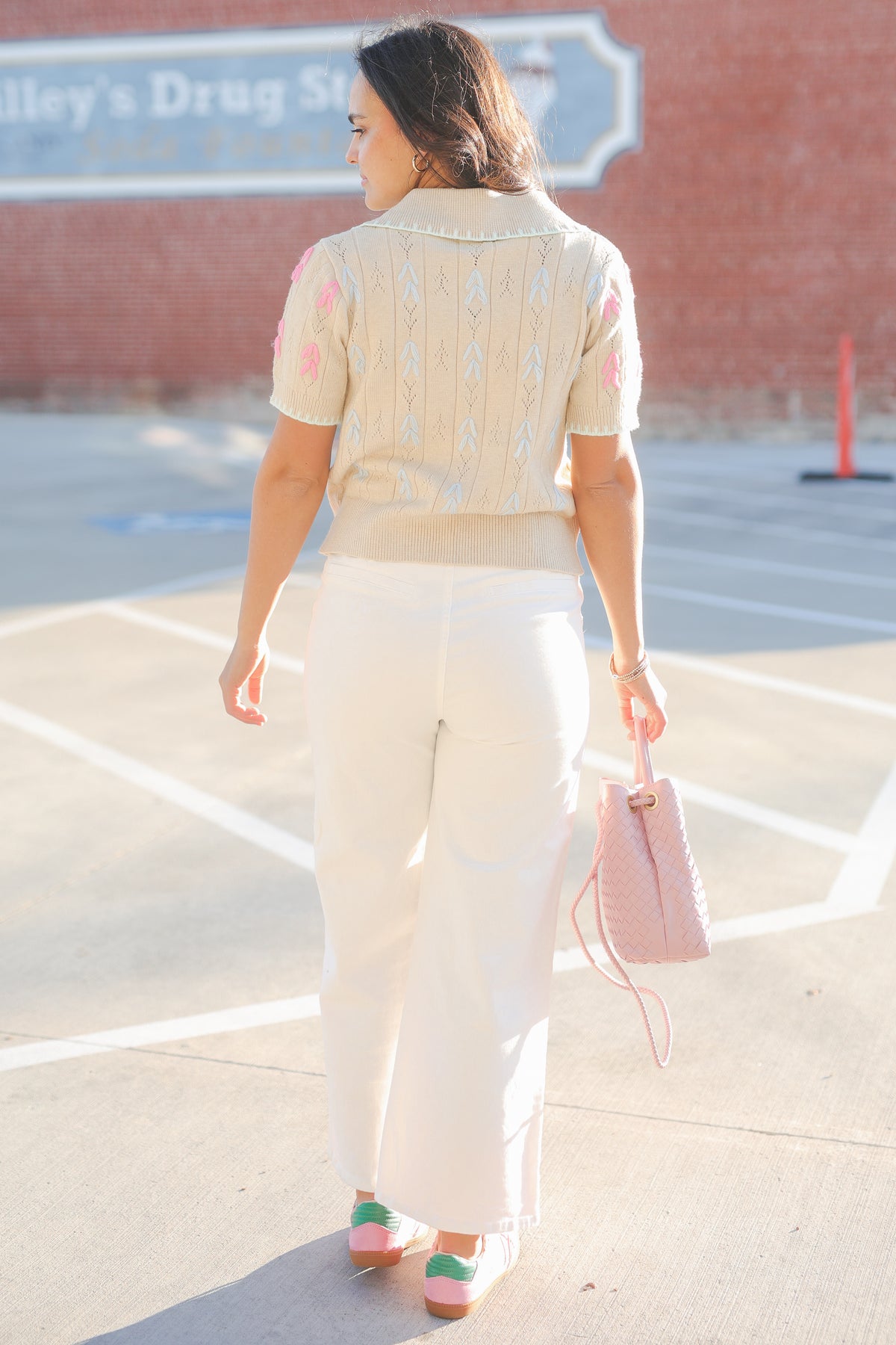 Woman in a light-colored outfit walking on a street with a pink handbag.