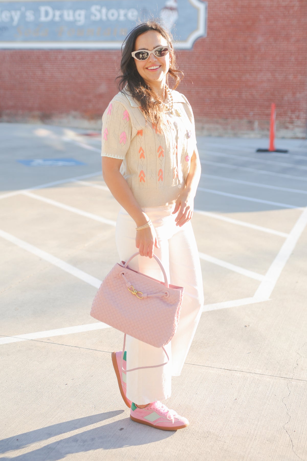 Woman holding a pink handbag in a parking lot with a brick building in the background.