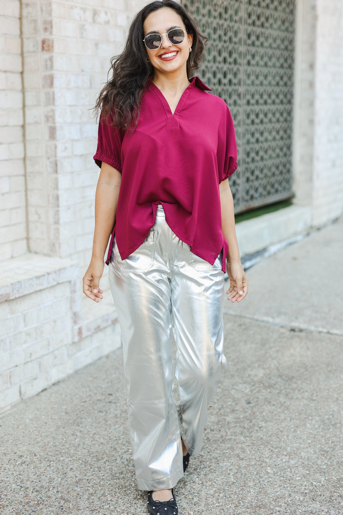 Woman wearing a magenta blouse and silver pants walking on a sidewalk.