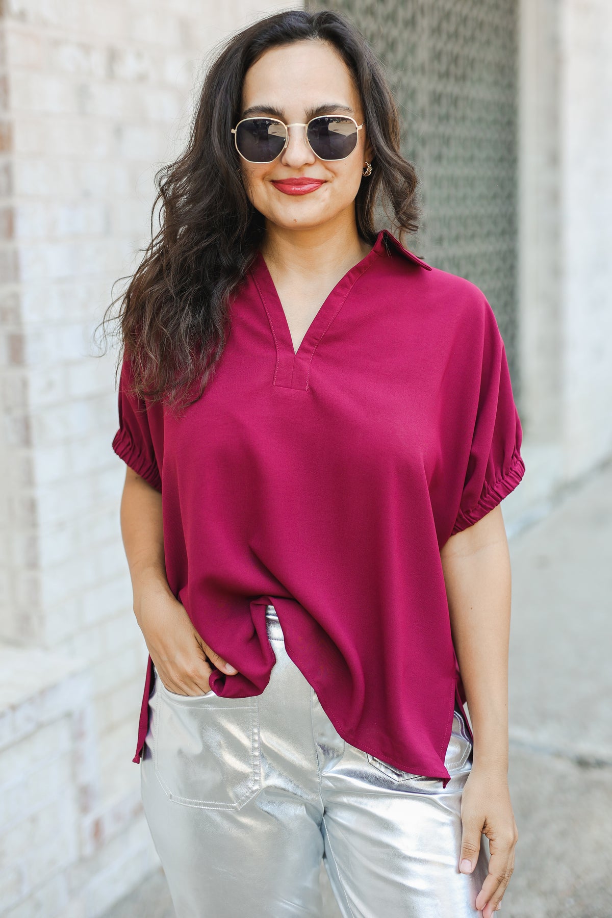 Woman wearing a magenta top and silver pants with sunglasses outdoors.