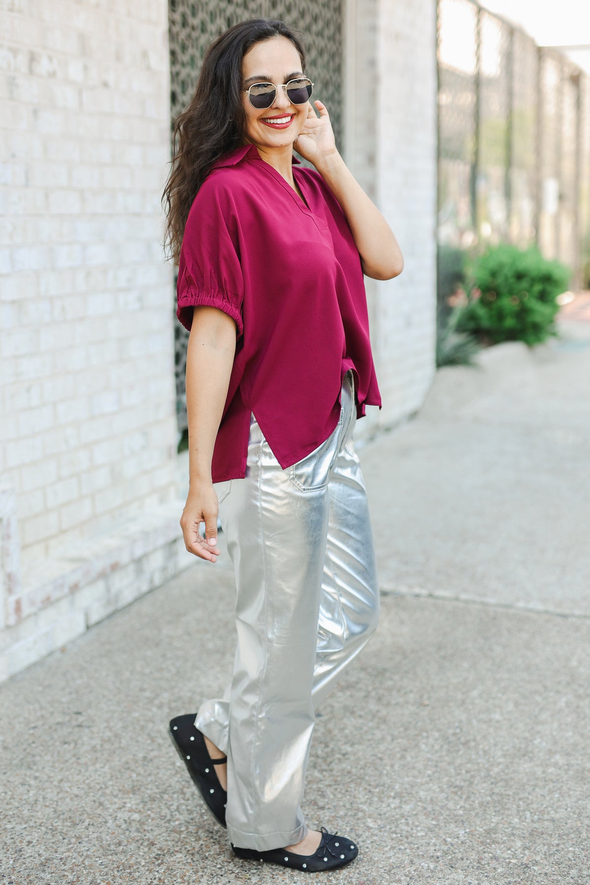 Woman wearing a magenta top and silver pants standing on a sidewalk.
