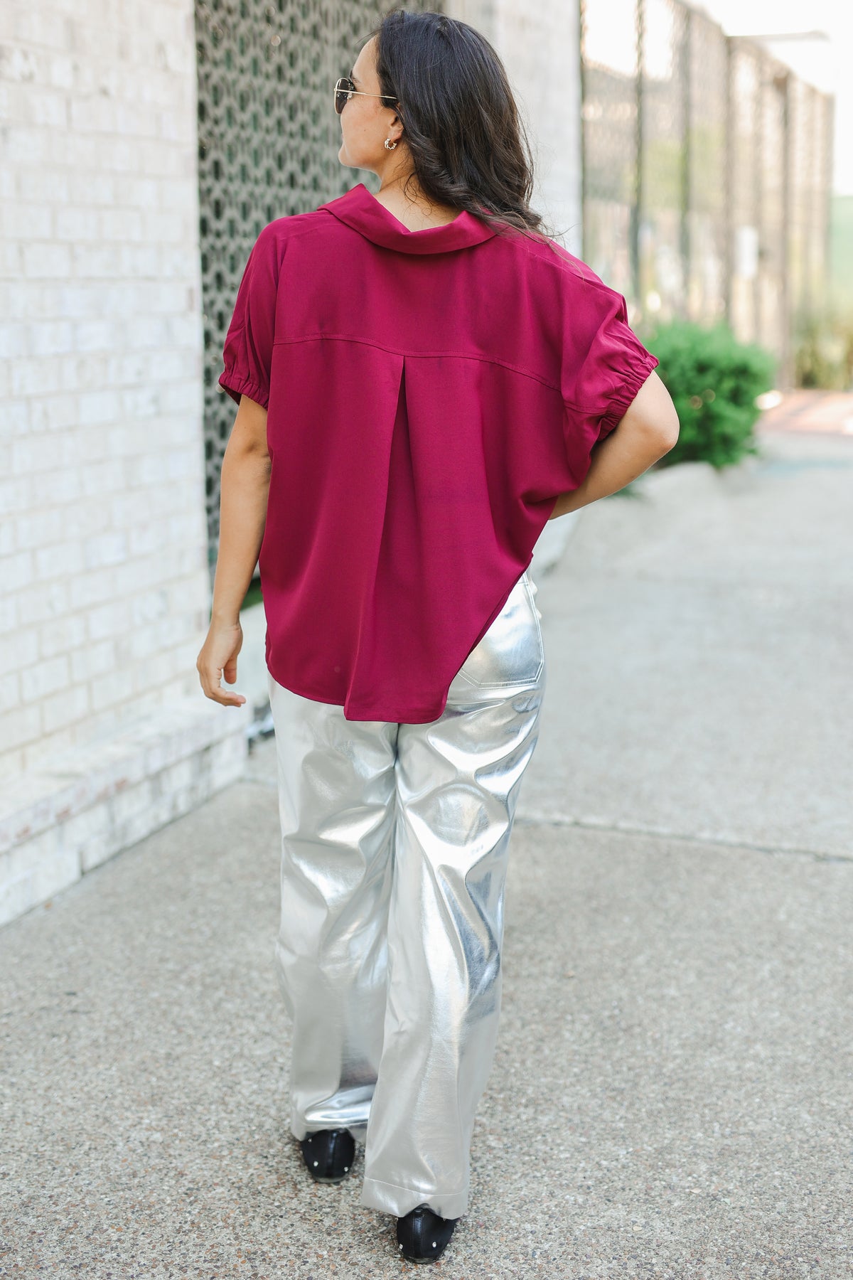 Person wearing a magenta top and silver pants walking on a sidewalk.
