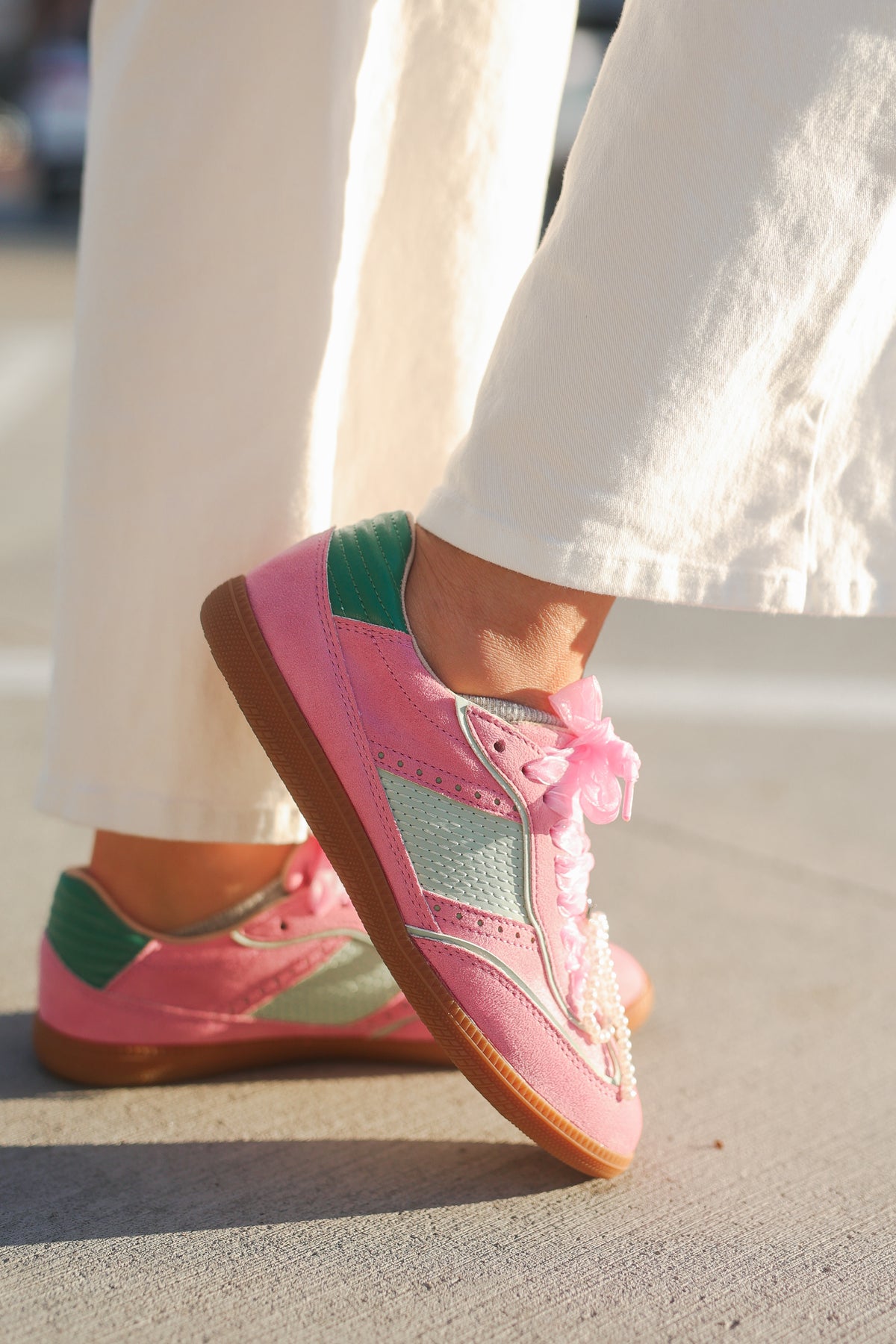 Pink sneakers with green accents worn by a person on a light-colored surface.