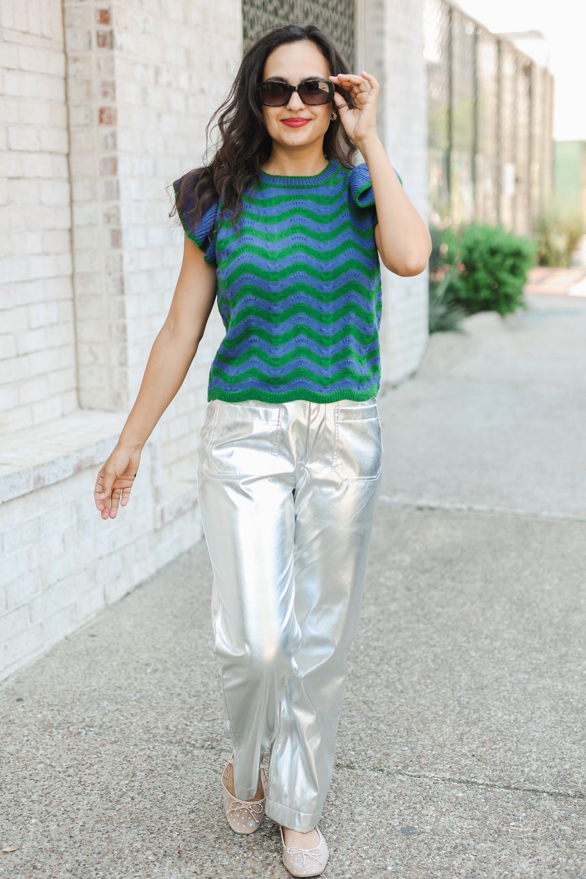 Woman wearing a green and blue striped shirt and silver pants walking outdoors.
