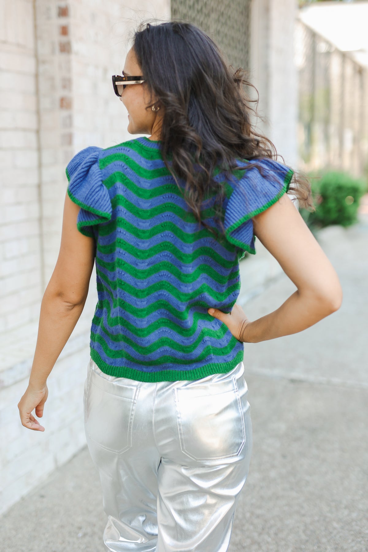 Woman wearing a blue and green patterned top with ruffled sleeves, walking outdoors.