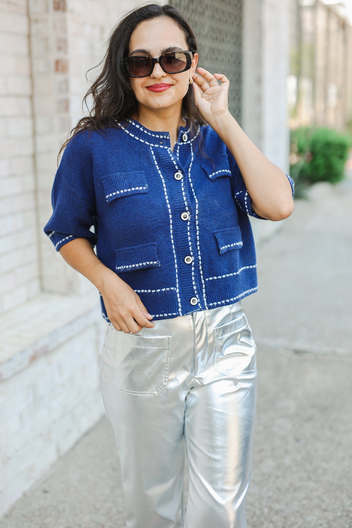 Woman wearing a blue jacket with white accents and silver pants on a sidewalk.