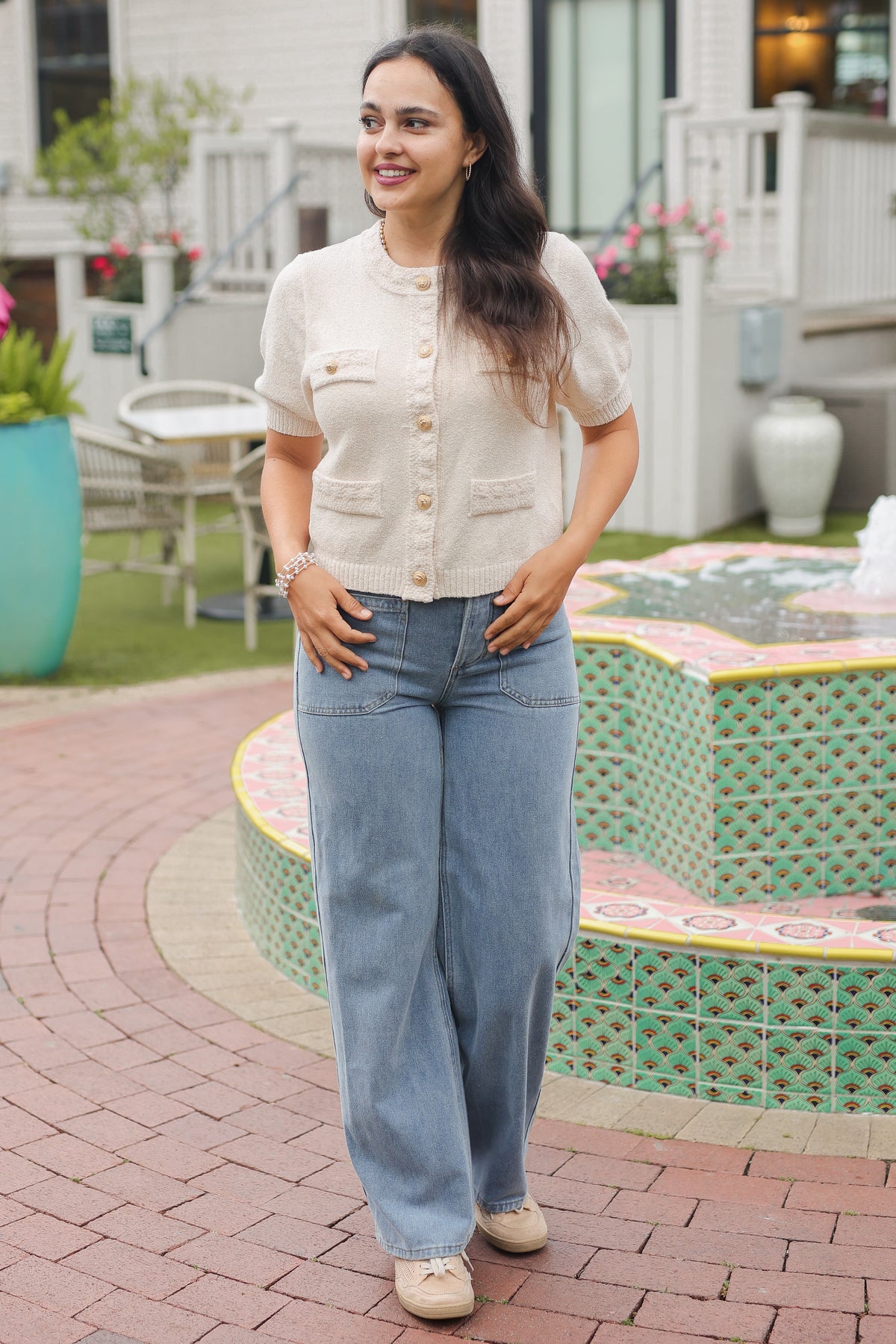 Woman in a white blouse and blue jeans standing in front of a fountain.