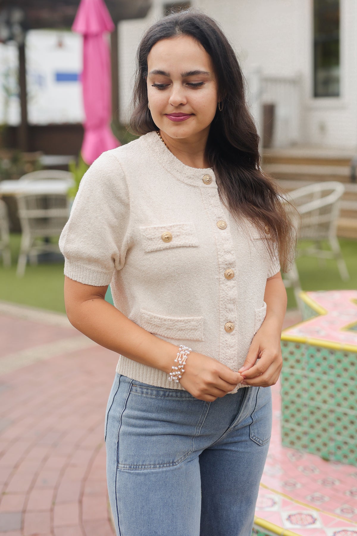 Woman wearing a cream-colored short-sleeve cardigan with gold buttons outdoors.