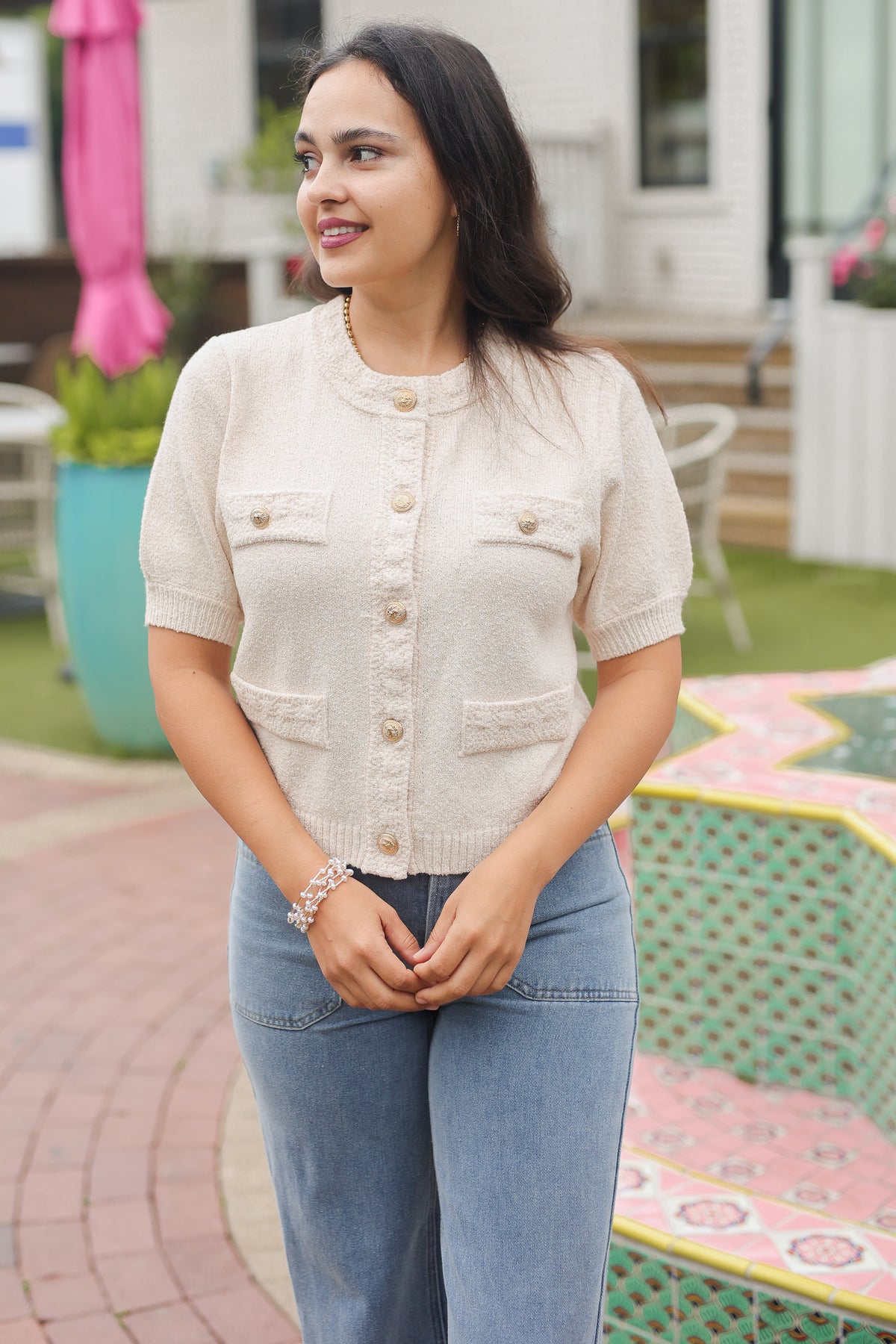 Woman wearing a beige cardigan and blue jeans standing outdoors.