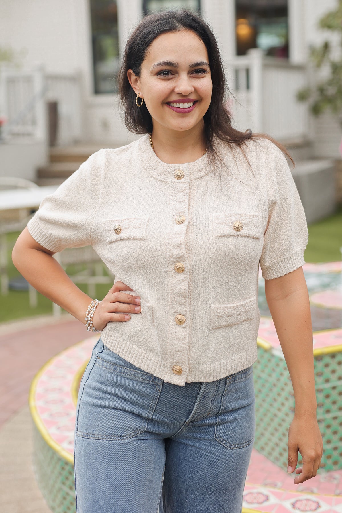 Woman wearing a cream cardigan and blue jeans standing outdoors.