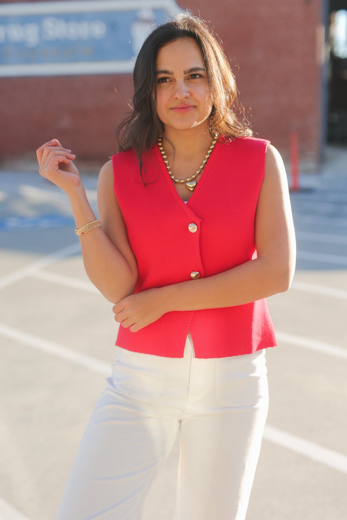 Woman wearing a red sleeveless top and white pants outdoors.