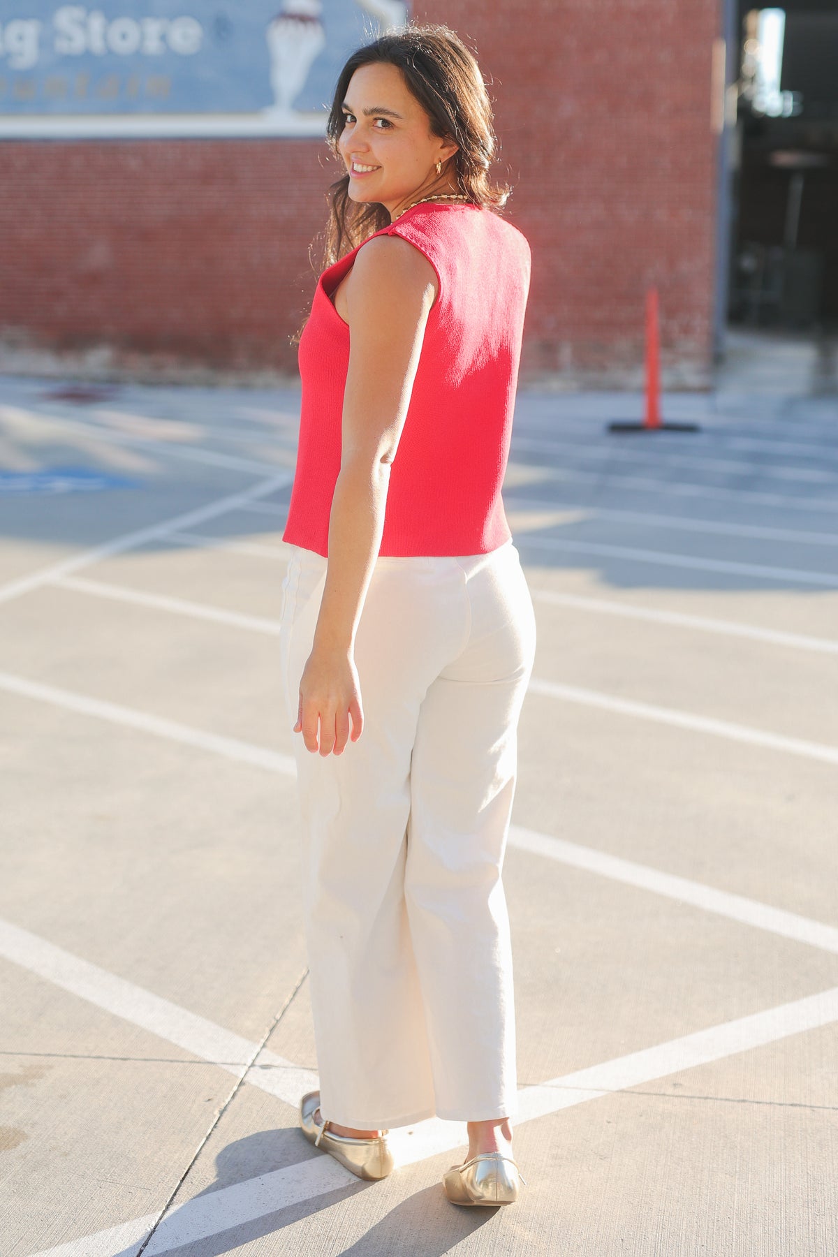 Woman in a red top and white pants standing in a parking lot.