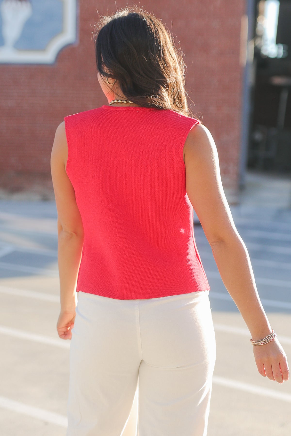 Person wearing a red sleeveless top and white pants walking on a street.