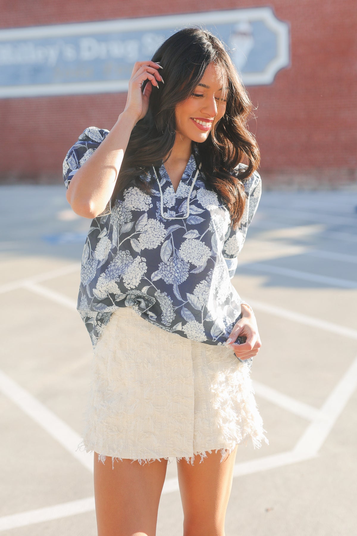 Woman wearing a blue floral blouse and white skirt outdoors.