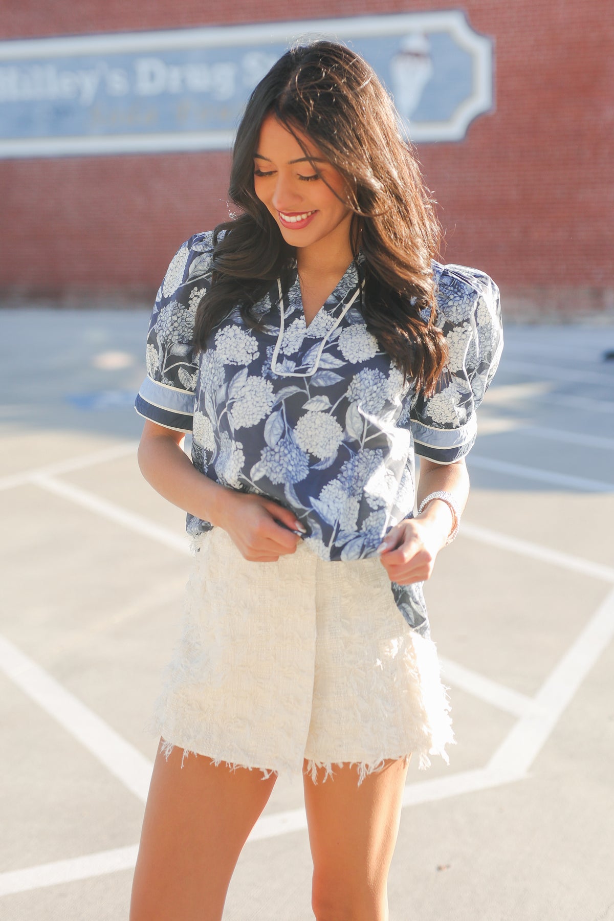 Woman wearing a blue floral blouse and white shorts standing on a basketball court.