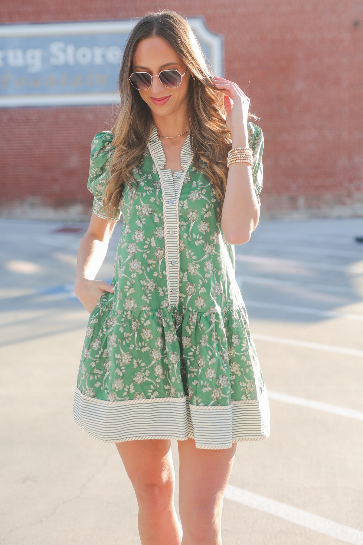 Woman wearing a green floral dress with a striped shirt underneath, standing in an outdoor setting.