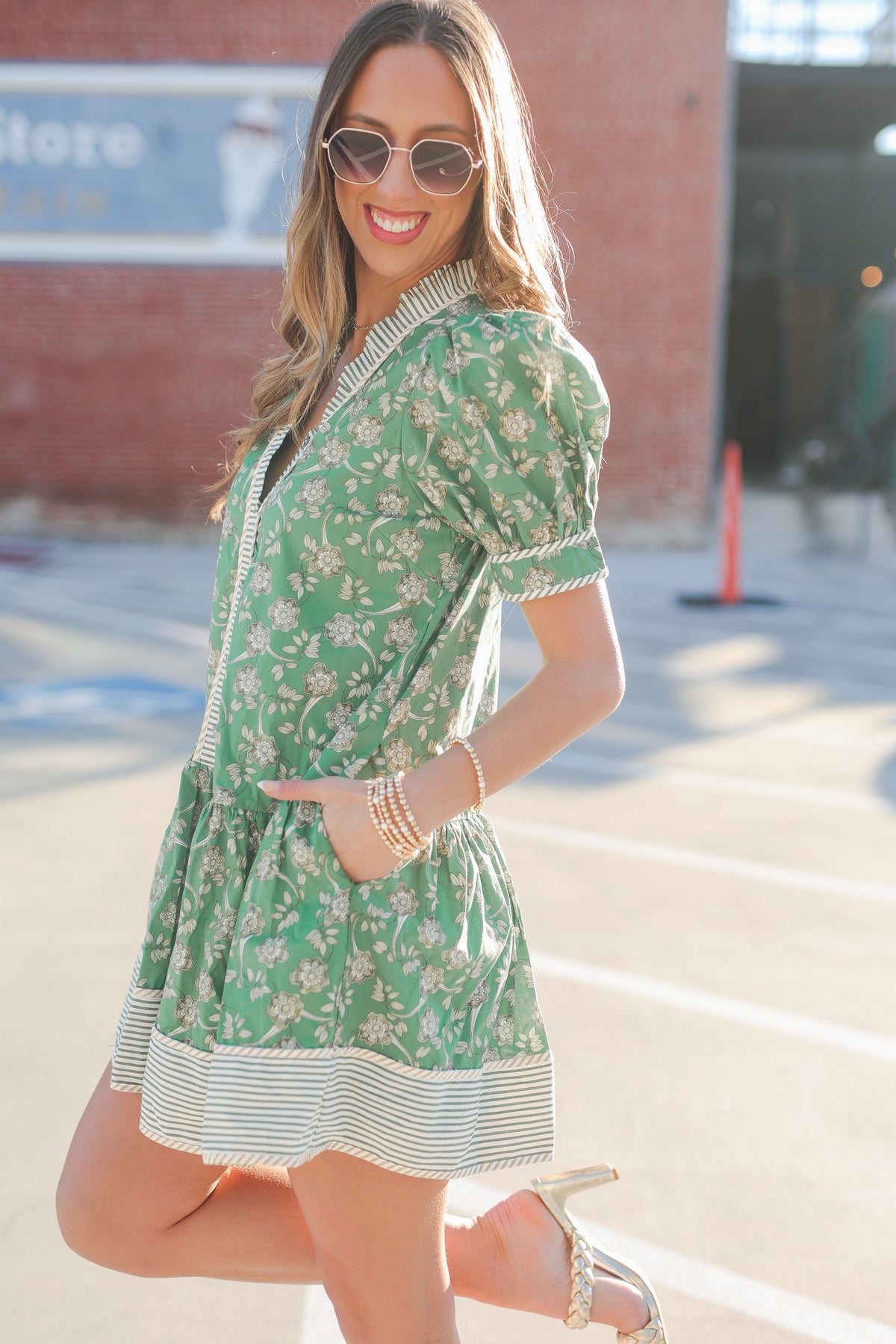 Woman wearing a green floral dress with sunglasses in an outdoor setting.