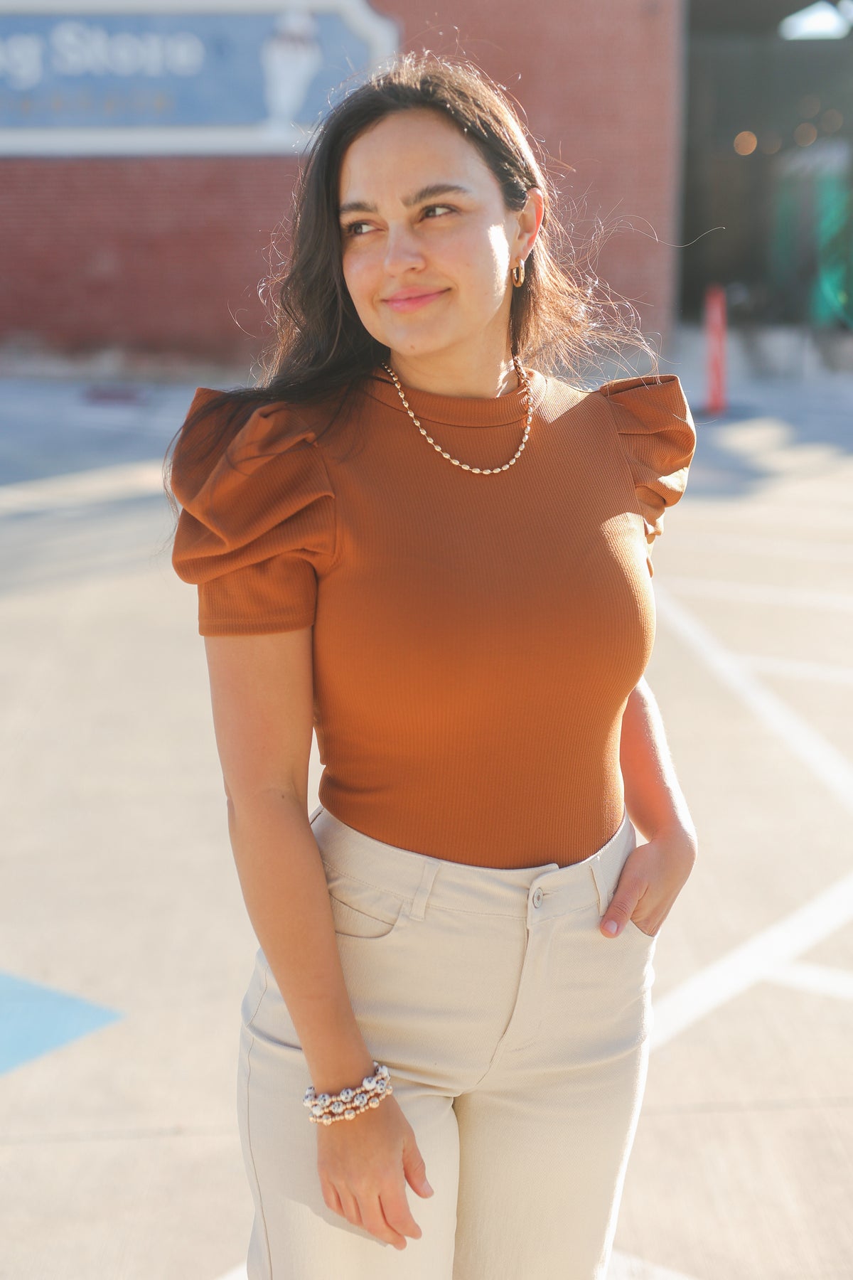 Woman wearing a brown top and white pants standing outdoors.