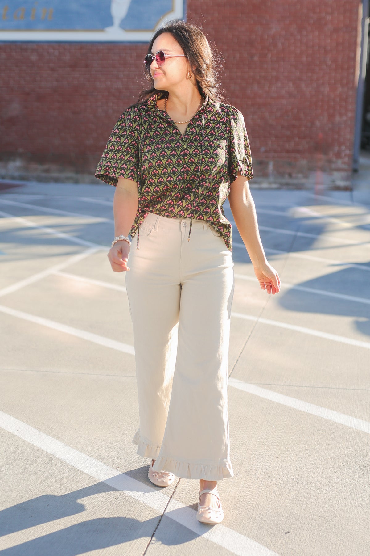 Woman wearing a patterned shirt and white pants on a basketball court.