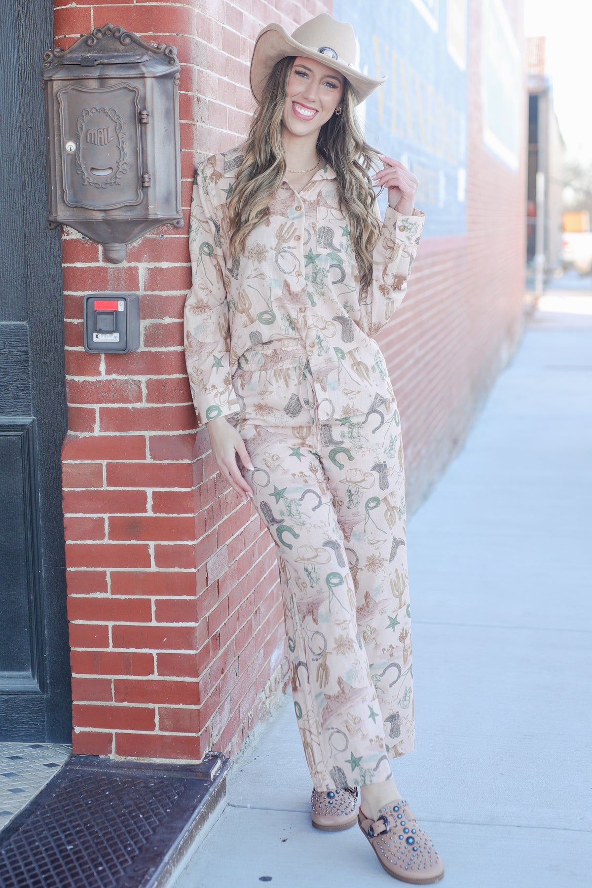 Woman in a floral outfit standing against a brick wall.