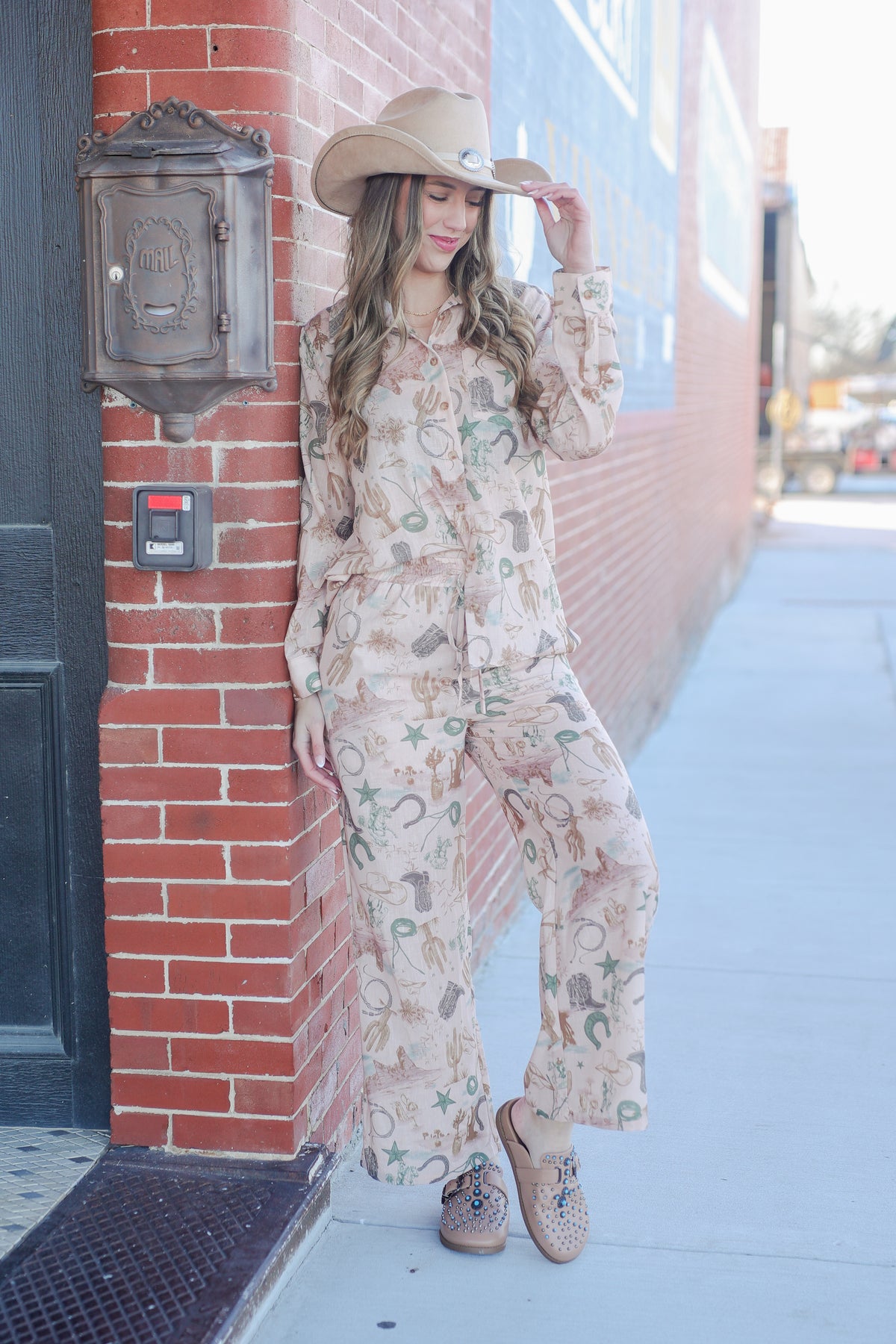 Woman in a patterned outfit standing against a brick wall on a city street.